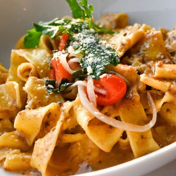 Close-up of Kai Eats + Drinks' Italian pasta dish with tomatoes, onions, and parmesan cheese.