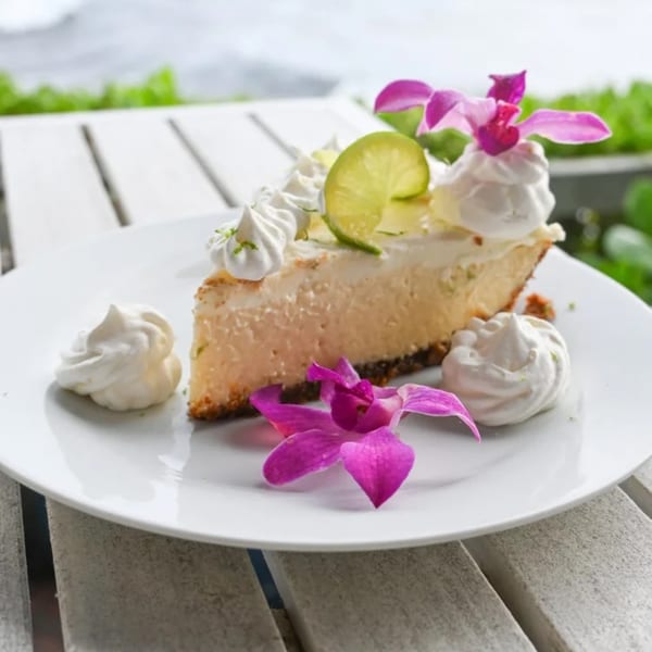 Slice of key lime pie with whipped cream, lime slices, and purple orchids on a white plate.