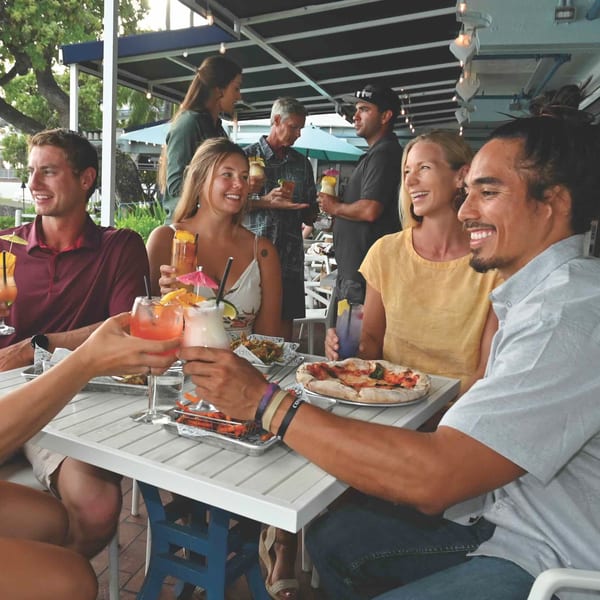 Friends enjoying cocktails, pizza, and appetizers at an outdoor restaurant table at Kai Eats + Drinks.