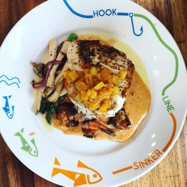 Seared fish with mango salsa, rice, shrimp, mushrooms, and asparagus on a decorative plate.