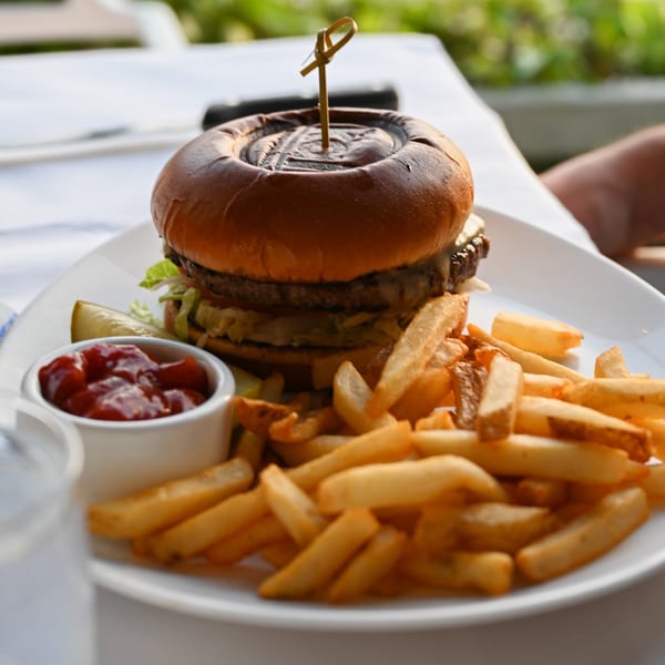 A Kai Eats + Drinks burger with fries, ketchup, and a pickle on a white plate.